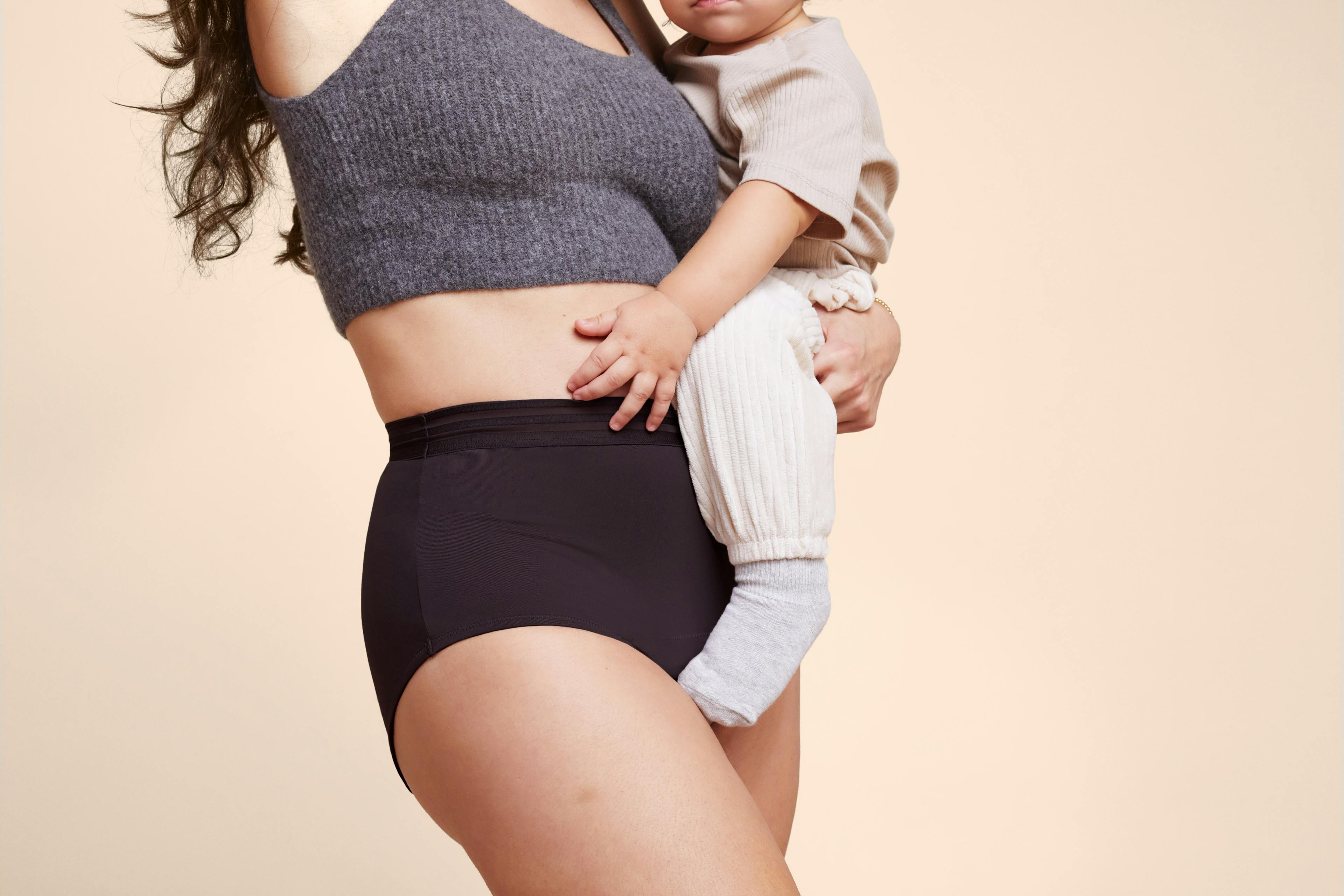 A photo of a woman wearing a pair of Thinx for All Leaks in the color black while holding a young child.