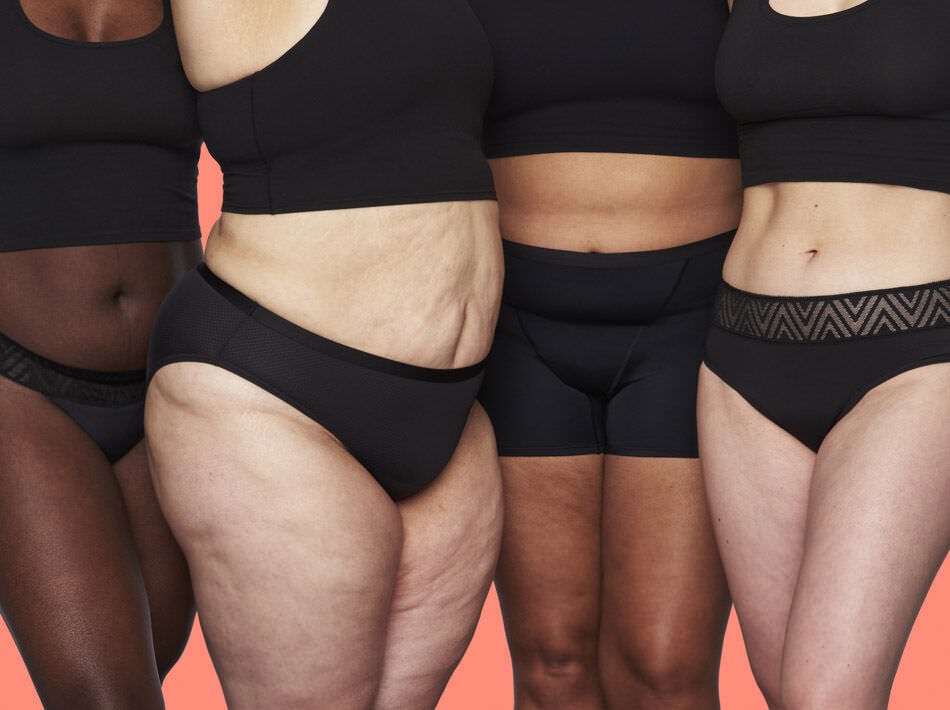 Four people standing in a row on a coral pink background, shown from the torso down, wearing black tank tops and black Thinx period underwear in the styles Hiphugger, air Bikini, Boyshort, and Thong